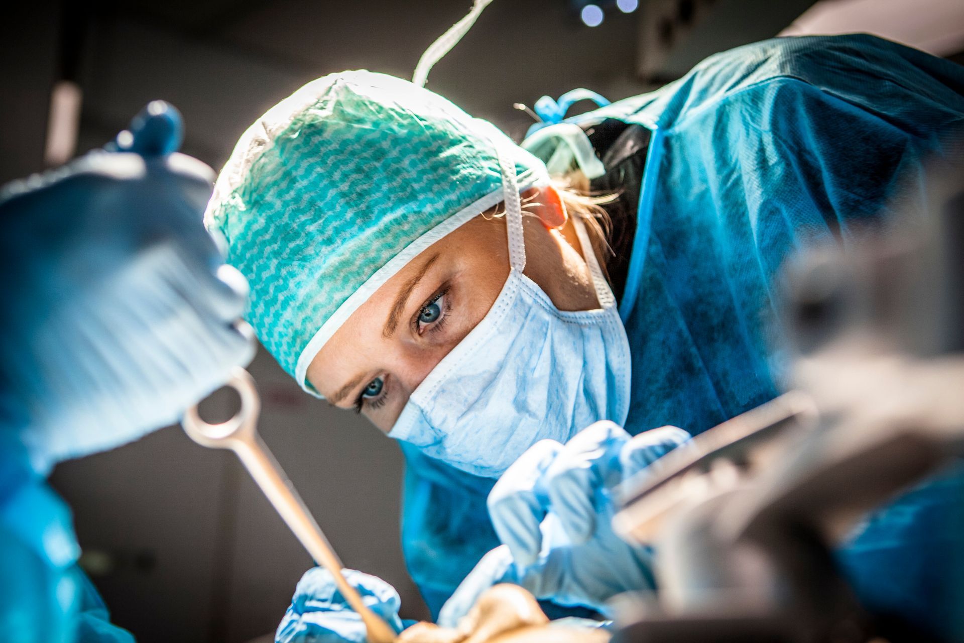 Photograph of two medical professionals wearing blue surgical scrubs, masks, and caps performing a dental procedure. Oral surgeon reviewing a dental X-ray with a patient before a surgical procedure