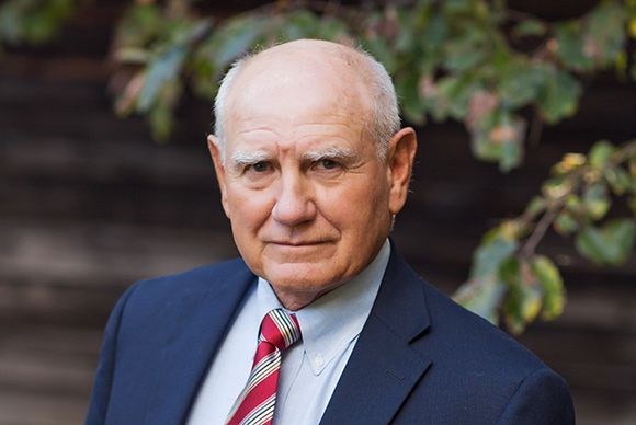 Lynn Blackburn in a suit and tie is standing in front of a tree.