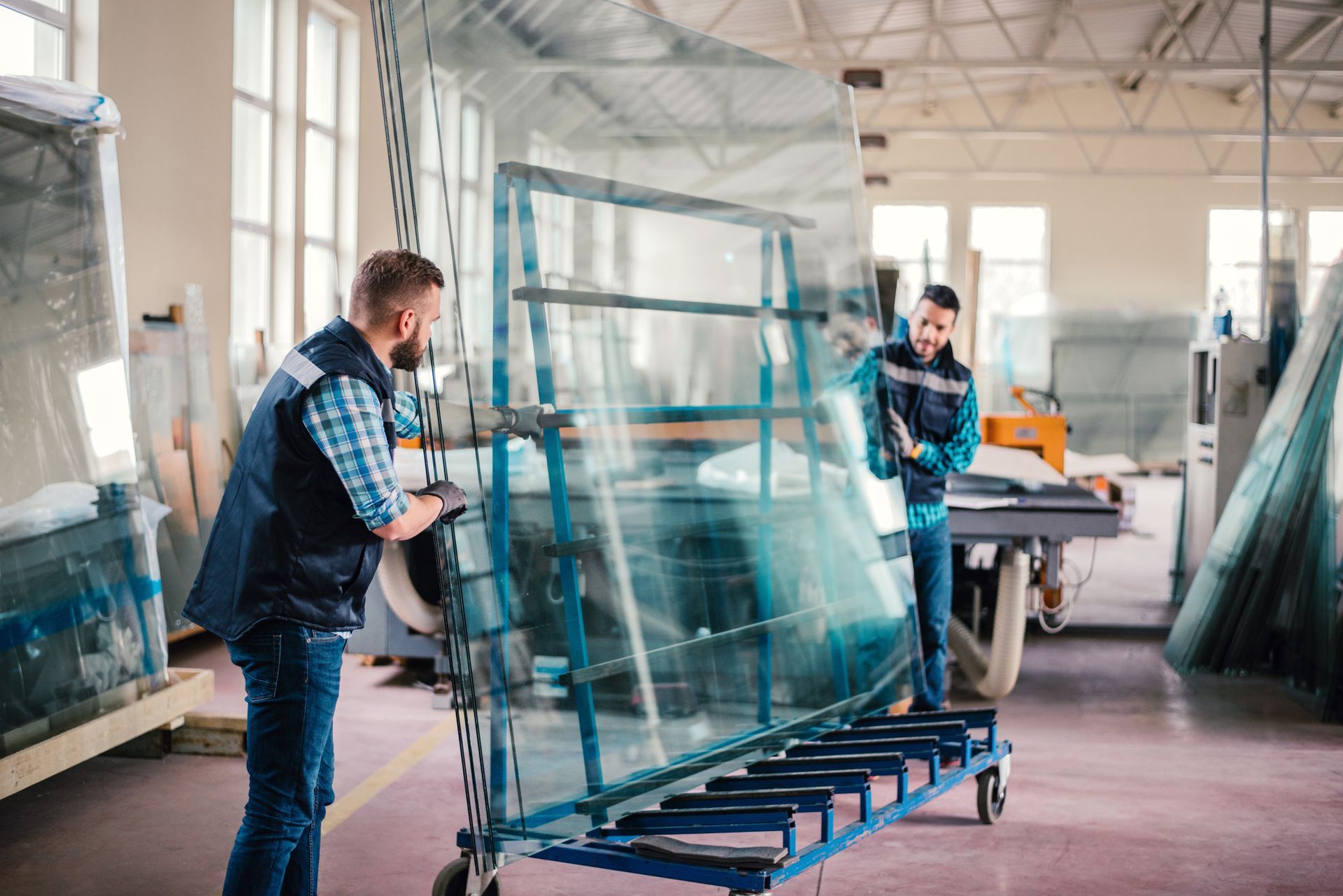 Two men are working on a large piece of glass in a factory.