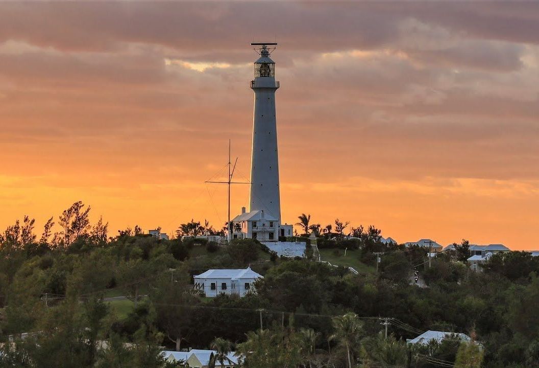 A lighthouse is sitting on top of a hill at sunset.