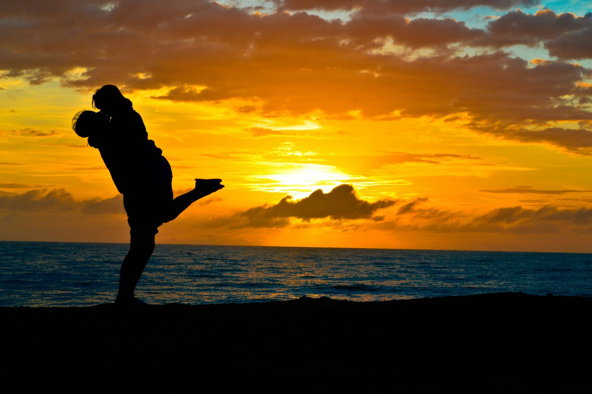 A man is holding a woman in his arms on the beach at sunset.