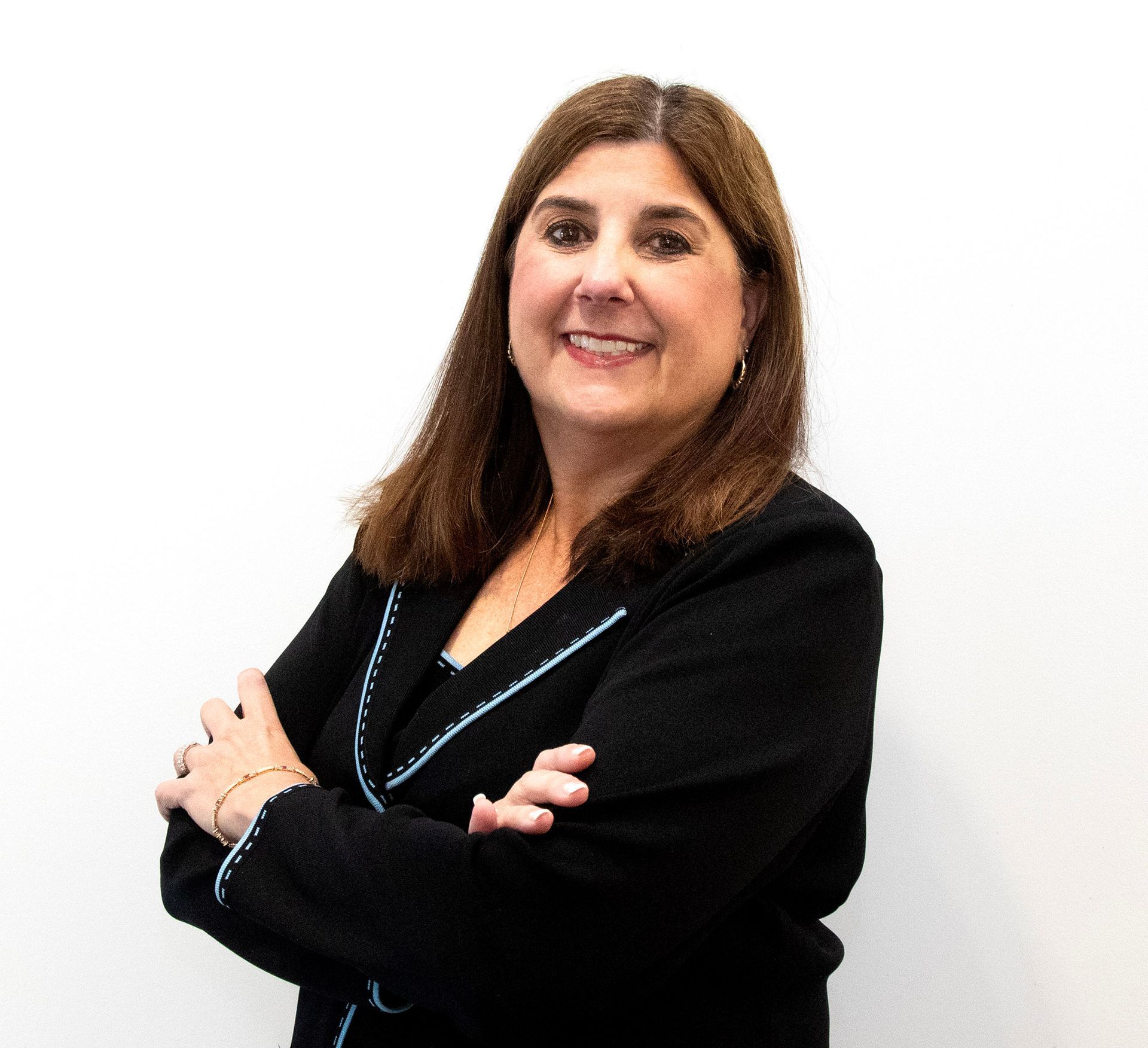 A woman in a black jacket is standing with her arms crossed and smiling.