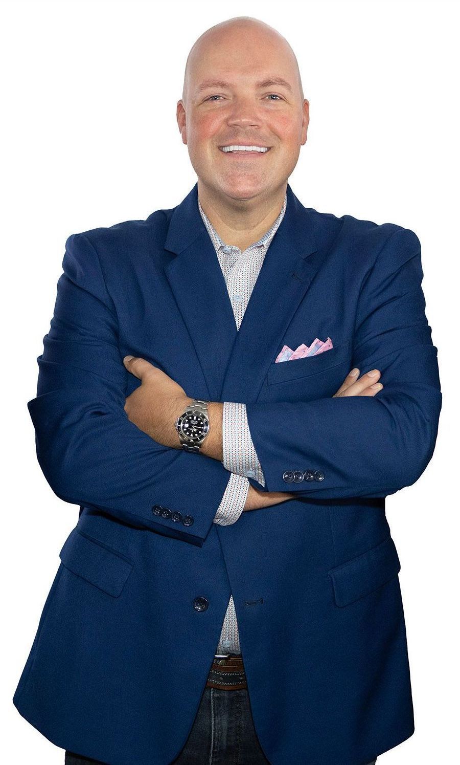 A man in a blue suit is standing with his arms crossed and smiling.