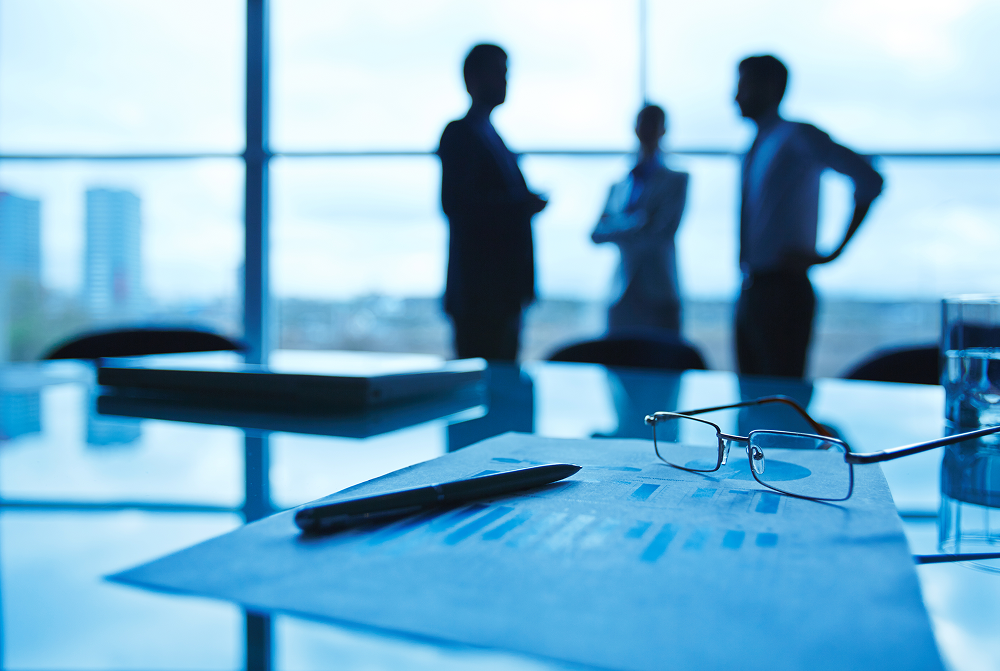 Business meeting silhouettes in a blue-tinted office, with papers and eyeglasses on the conference table