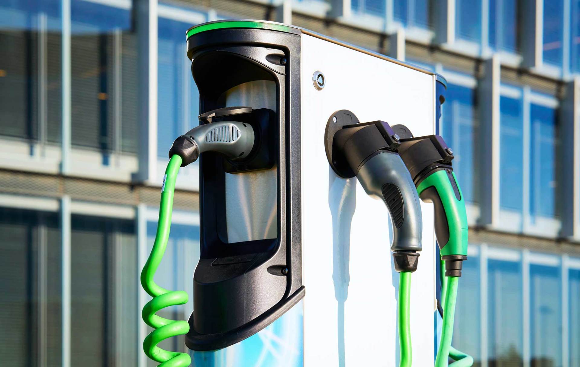 Una stazione di ricarica per veicoli elettrici con tre cavi di ricarica verde brillante collegati all'unità.