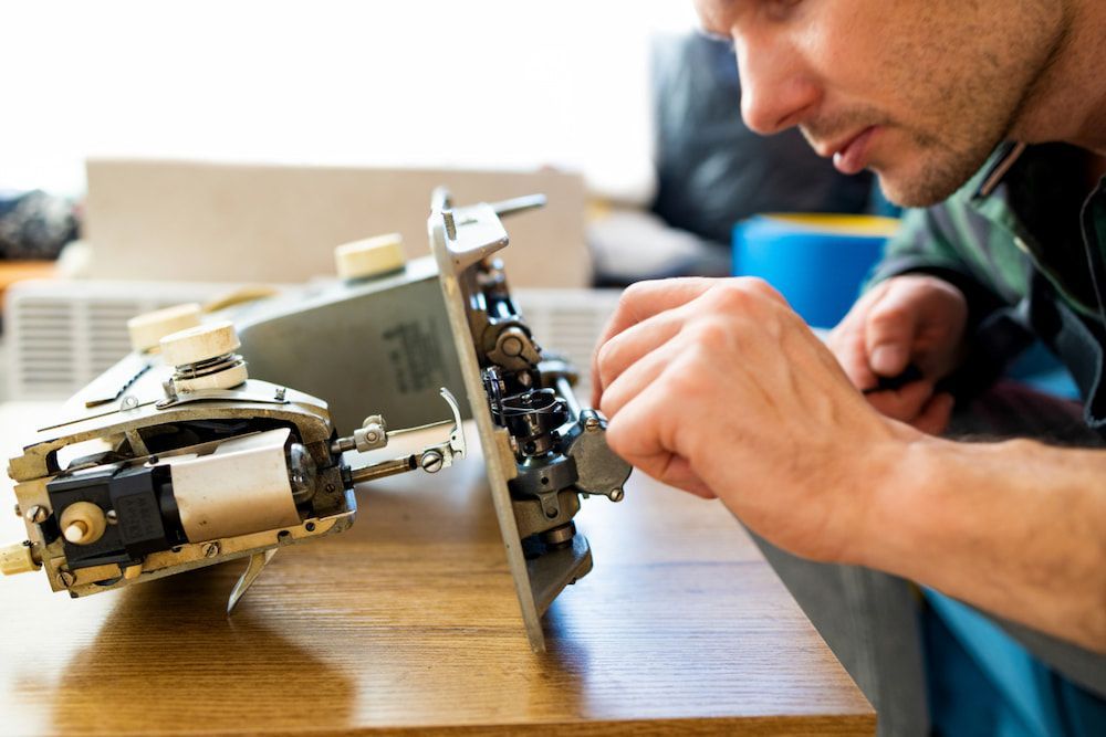 A Man is Working on a Sewing Machine on a Wooden Table — James Hunter Mobile Sewing Machine Mechanic in Battery Hill, QLD
