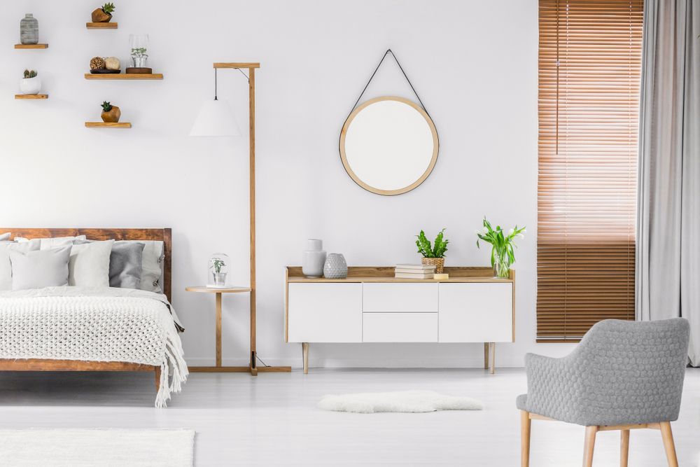 Um quarto com uma cama, cômoda, cadeira e espelho.
