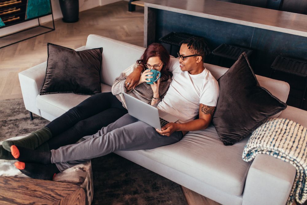 Um homem e uma mulher estão sentados em um sofá usando um laptop.