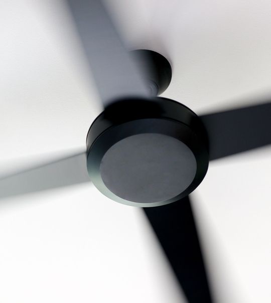 Um ventilador de teto preto está girando em um fundo branco