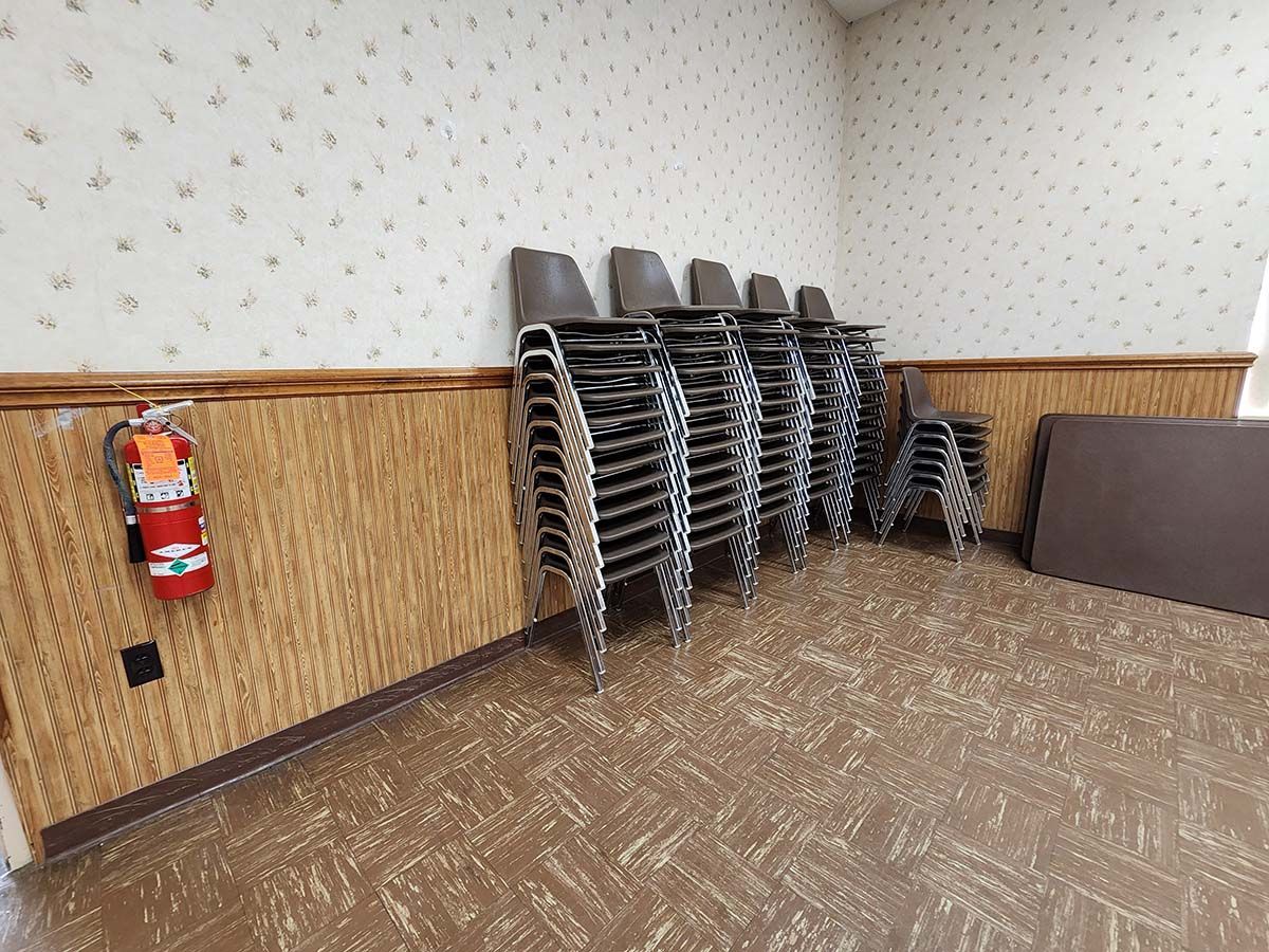 Stacked metal chairs in an empty room with patterned wallpaper and a wall-mounted fire extinguisher