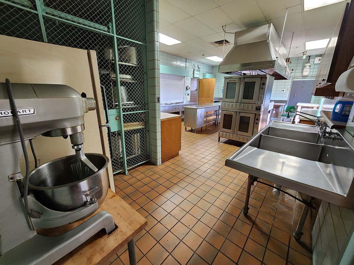Commercial kitchen with stainless-steel appliances, tiled floor, and a large mixer in the foreground