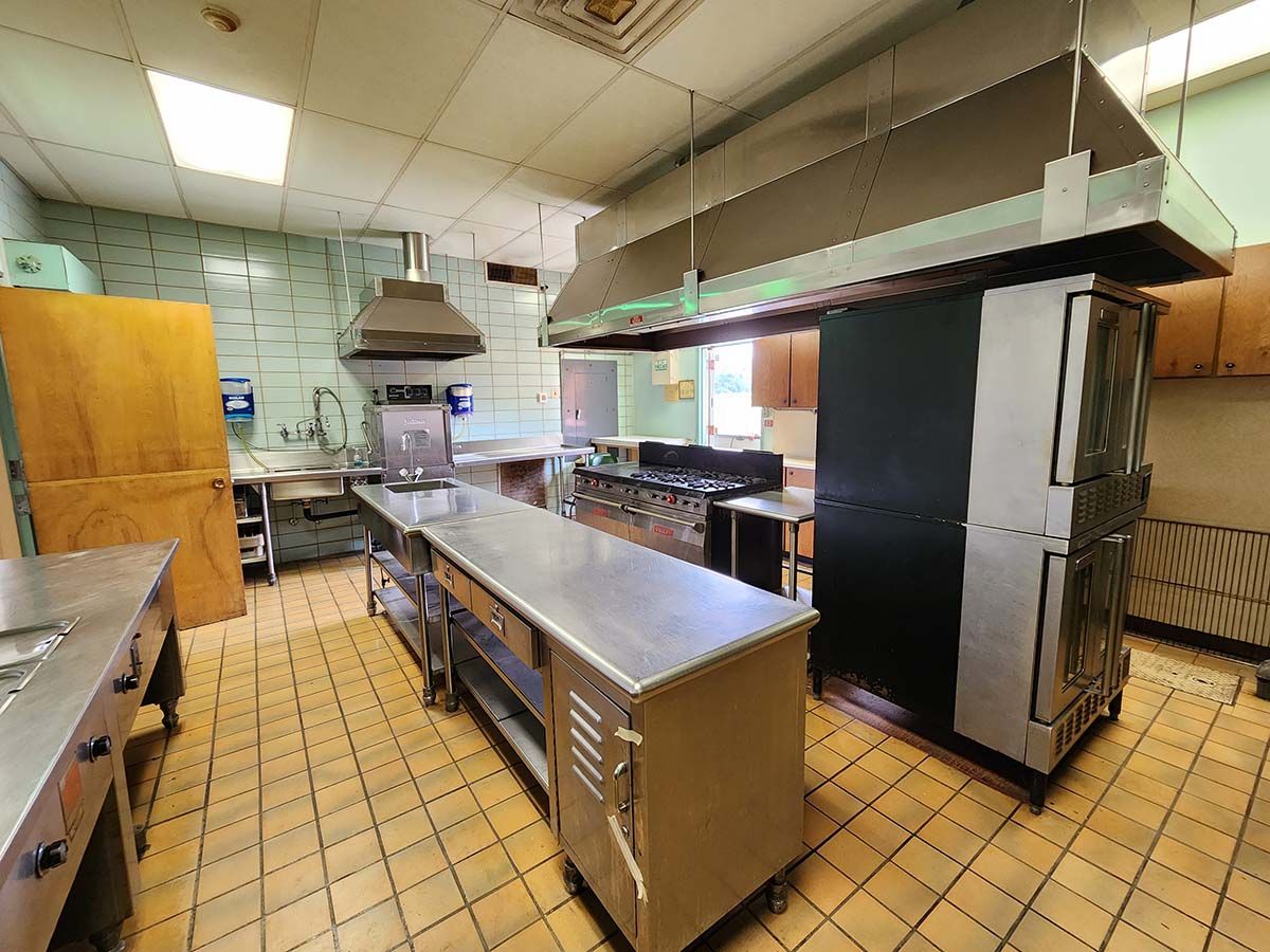Commercial kitchen with stainless steel counters, large hood vents, and tiled floor.