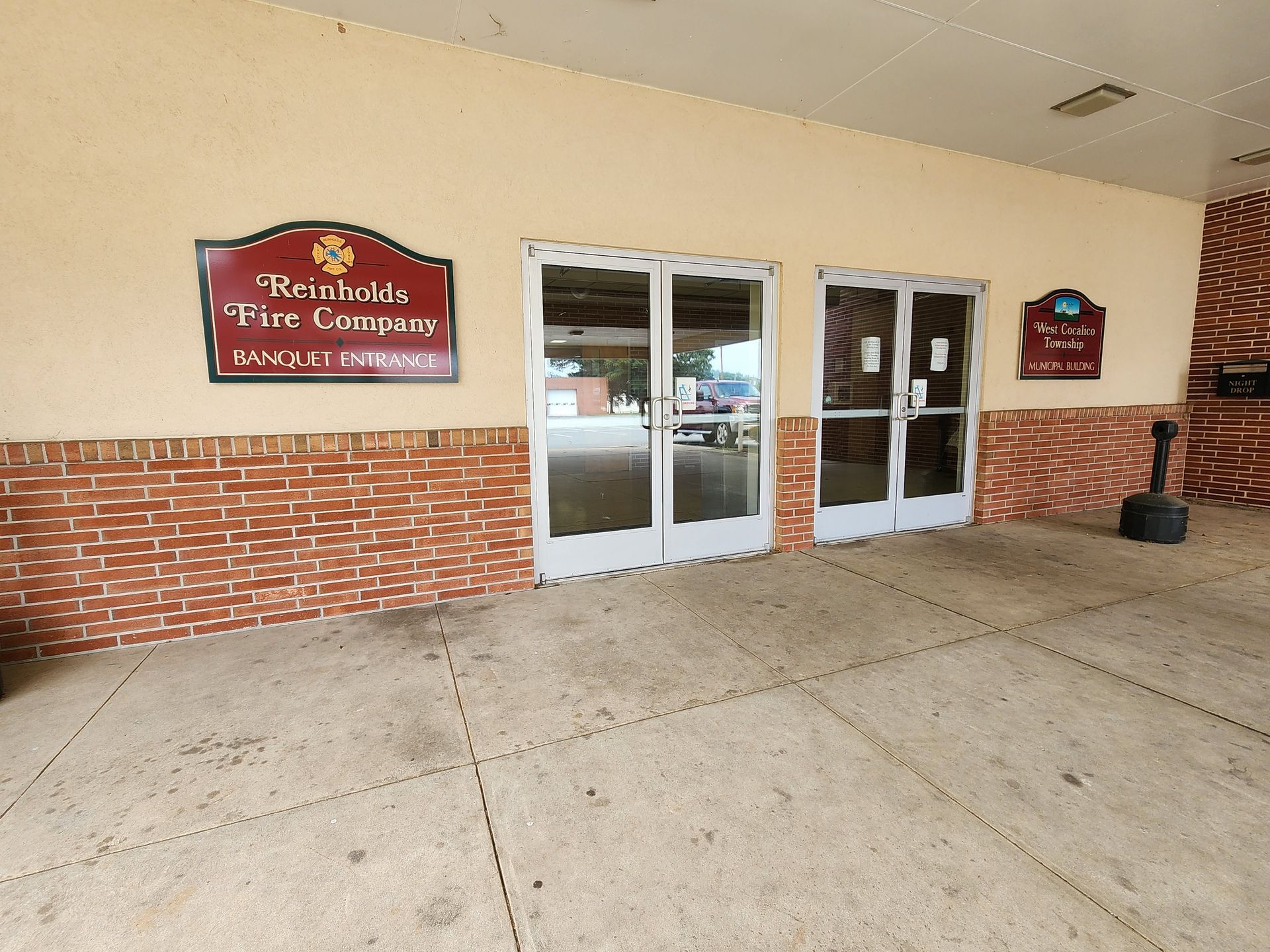 Storefront entrance with red-and-white brick facade and glass double doors beneath a covered walkway