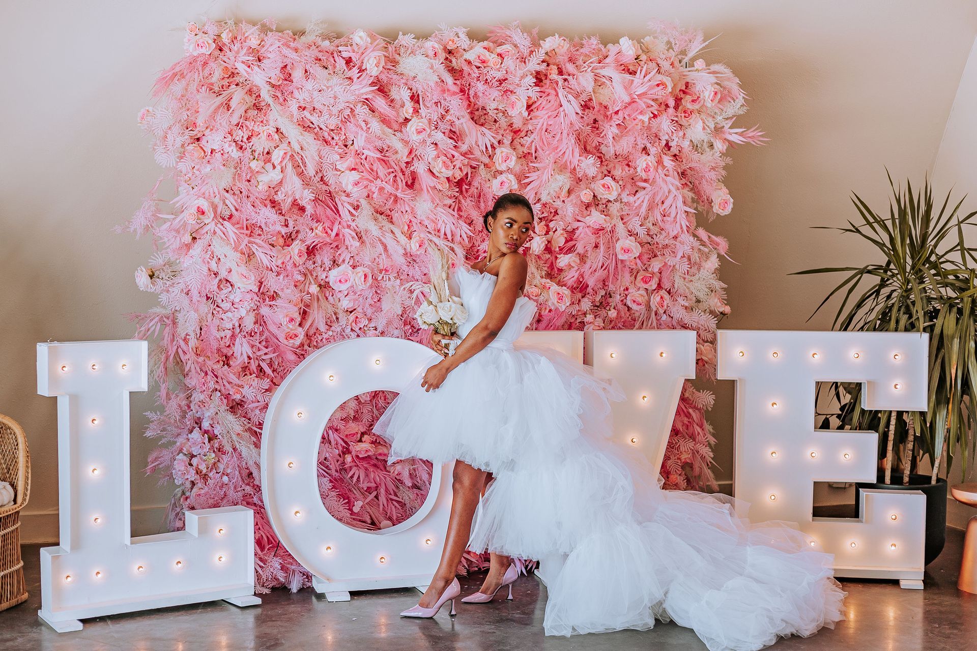 A bride in a white dress is standing in front of a wall of pink flowers.