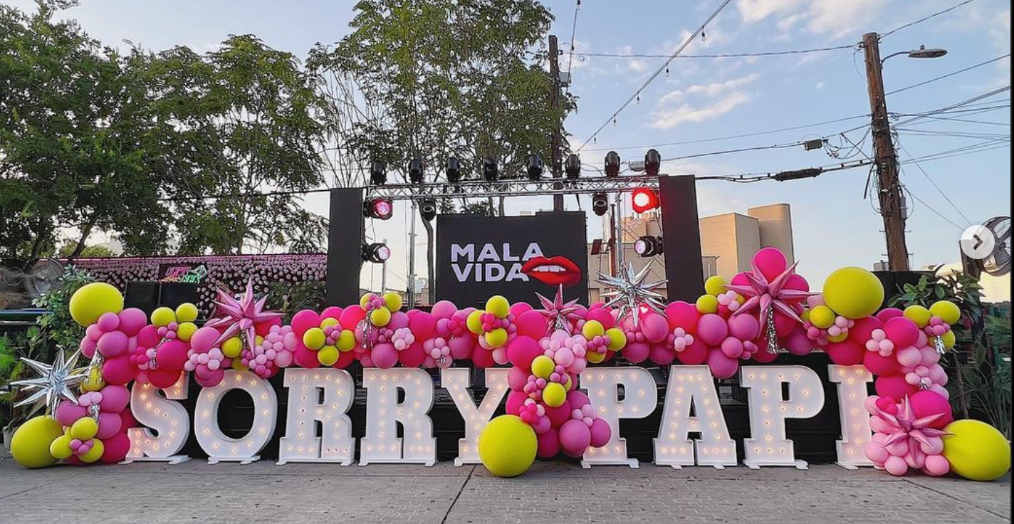 A sign that says sorry papi is surrounded by pink and yellow balloons