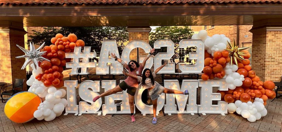 A couple of people standing in front of a sign made of balloons.