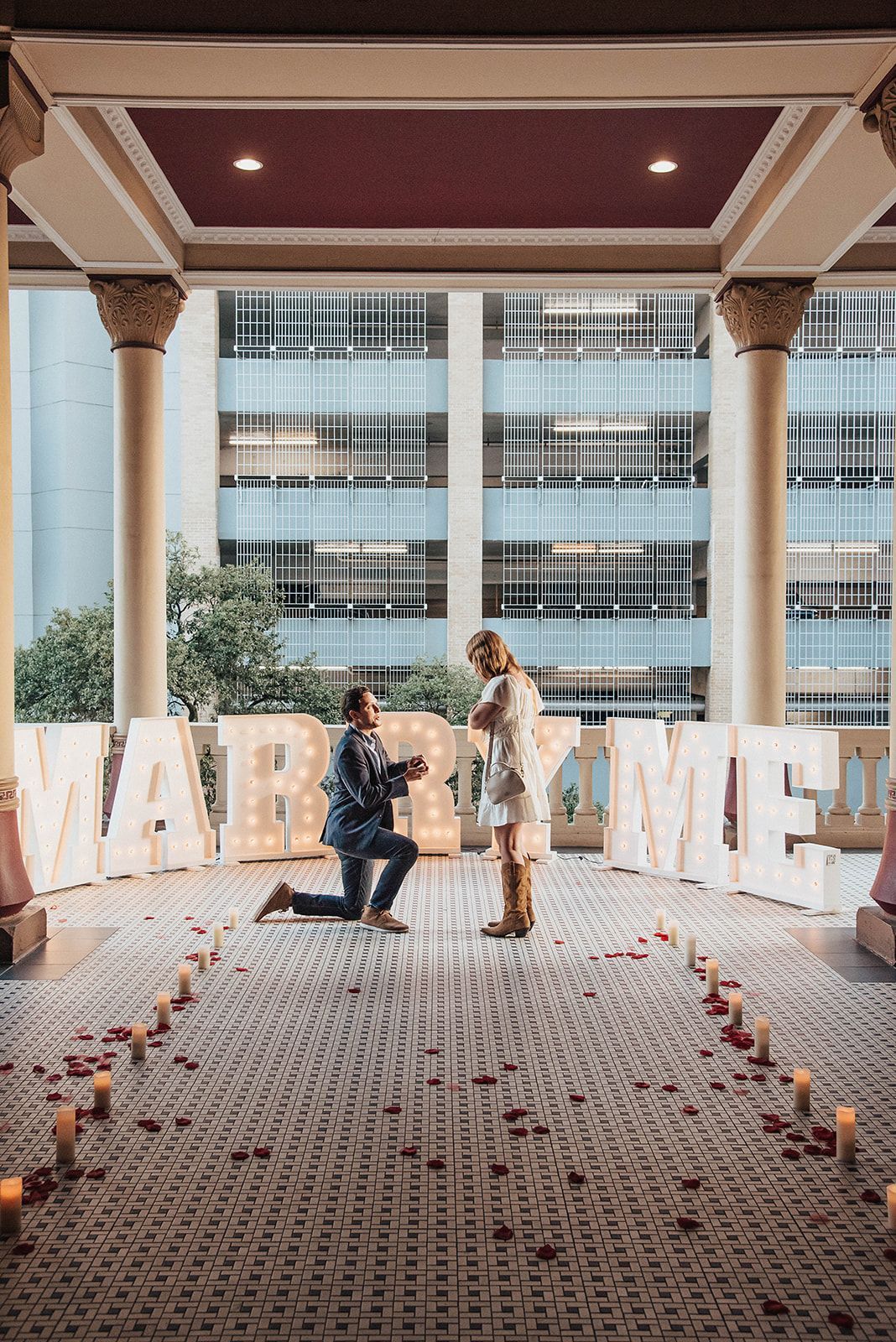A man is kneeling down in front of a sign that says marry me.