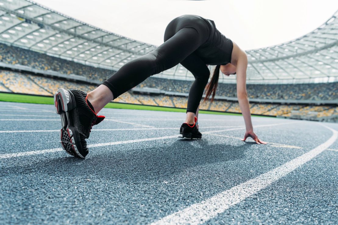 Un corridore in posizione di partenza su una pista di uno stadio, pronto a scattare.