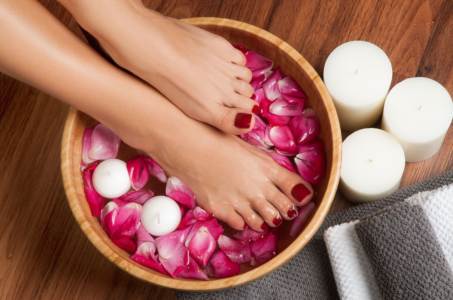 Feet soaking in a wooden bowl filled with rose petals and candles for a spa treatment. Feet soaking in a wooden bowl filled with rose petals and candles for a spa treatment.