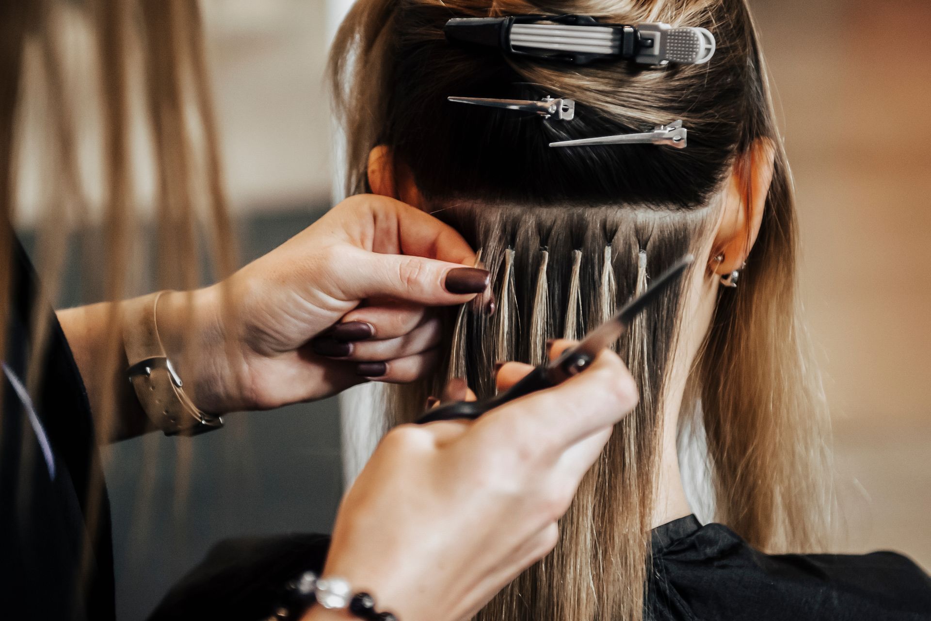 Stylist applying hair extensions to blonde hair in a salon setting. A hairdresser does hair extensions for a blonde girl in a hair salon.