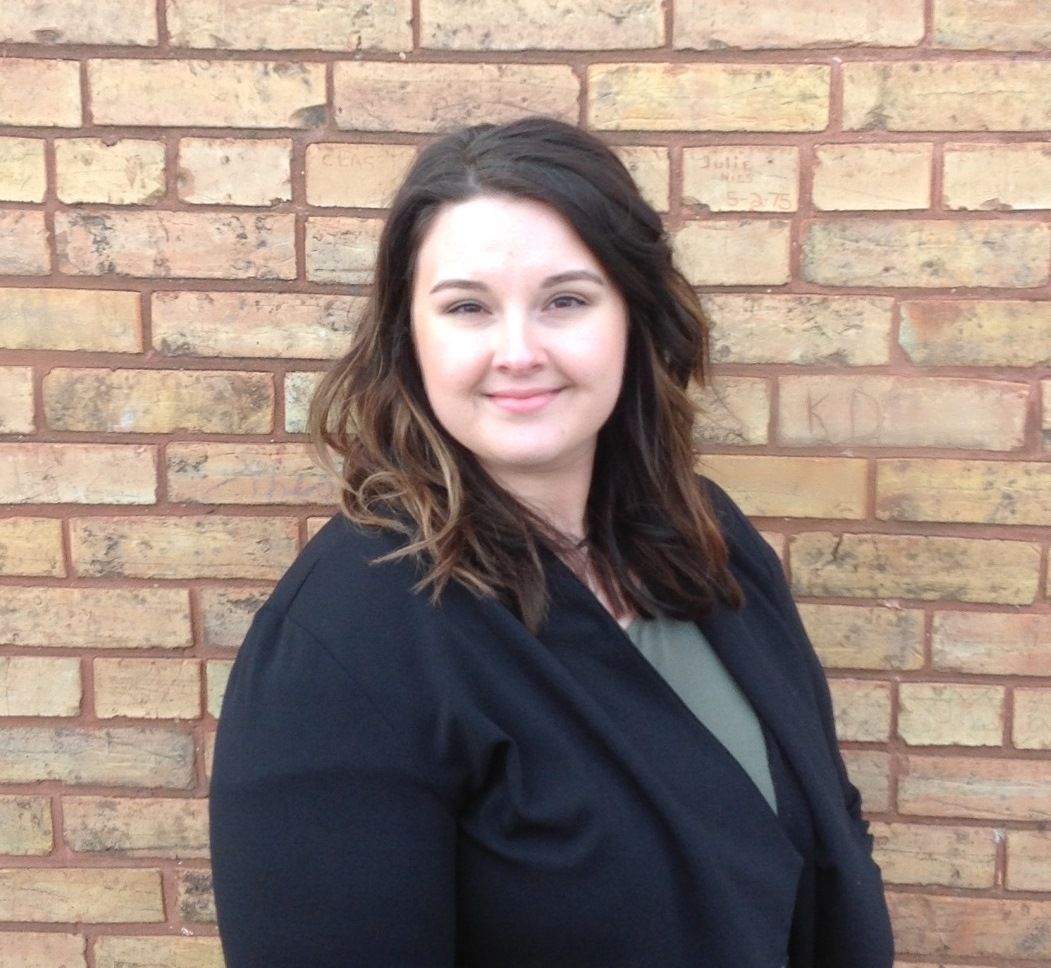 Woman in a black cardigan smiles in front of a brick wall.