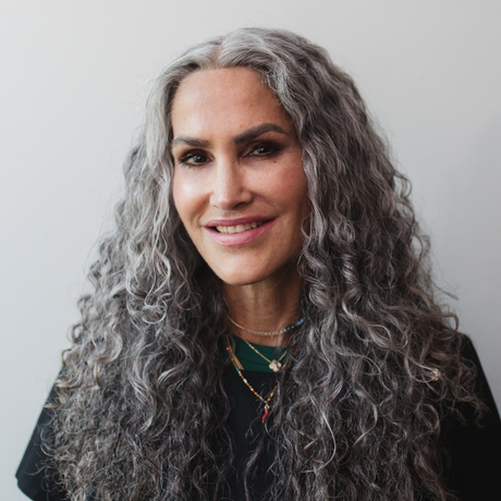 A woman with long curly gray hair is smiling for the camera.