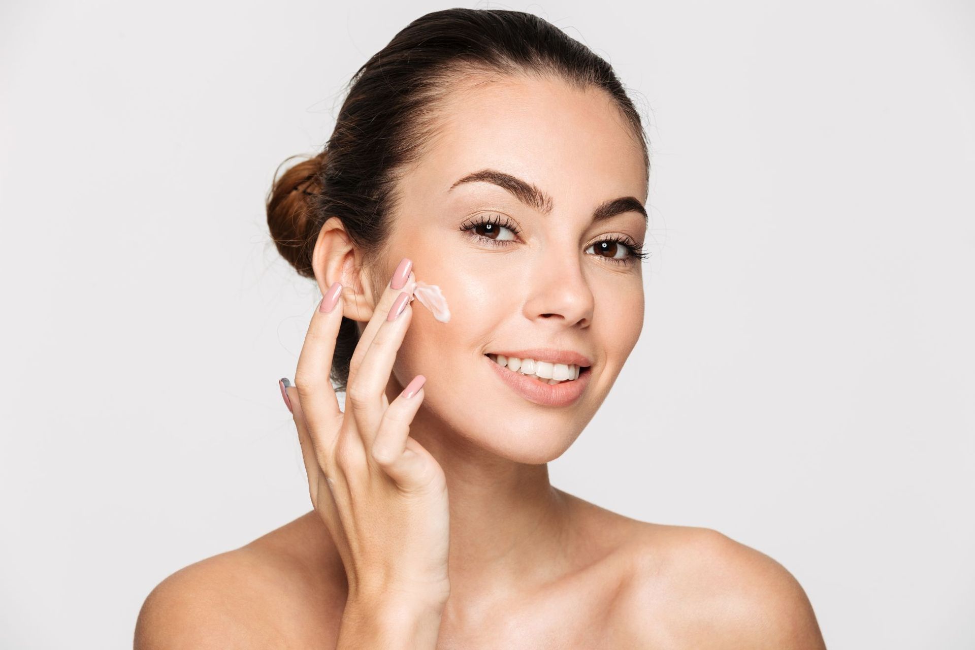 A woman is smiling while applying cream to her face.