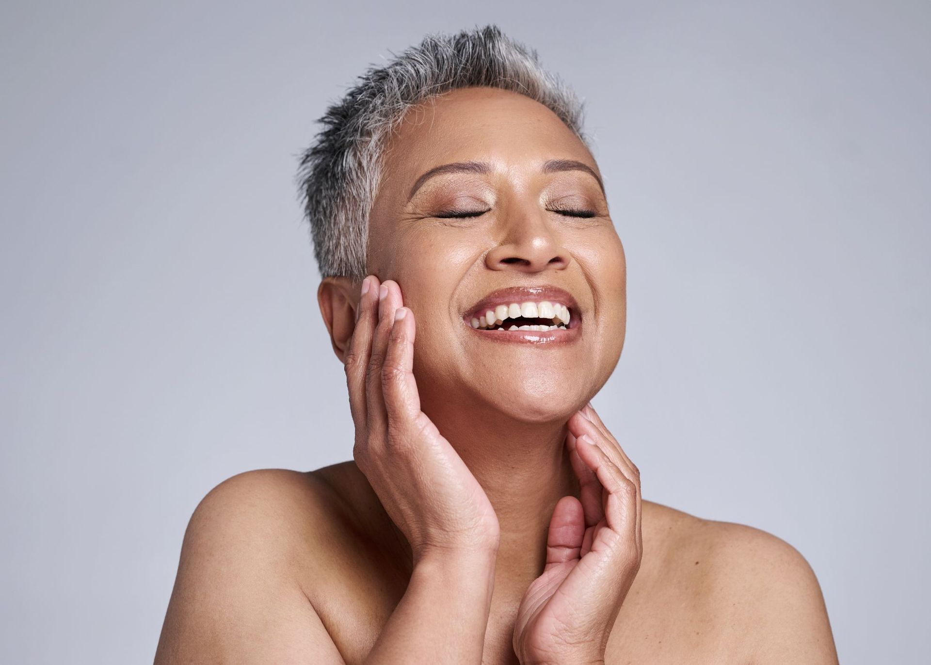 An older woman is smiling and touching her face with her hands.