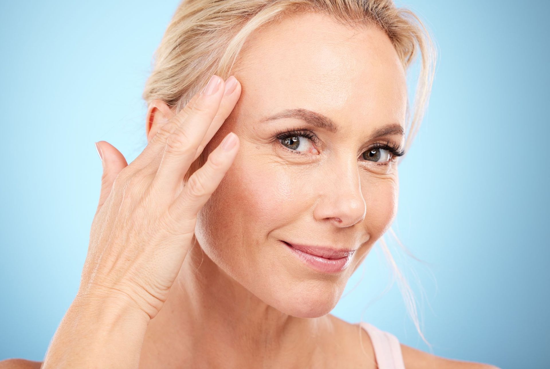 A woman is touching her face with her hand and smiling.