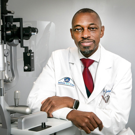 A man in a white coat and red tie is sitting in front of a machine