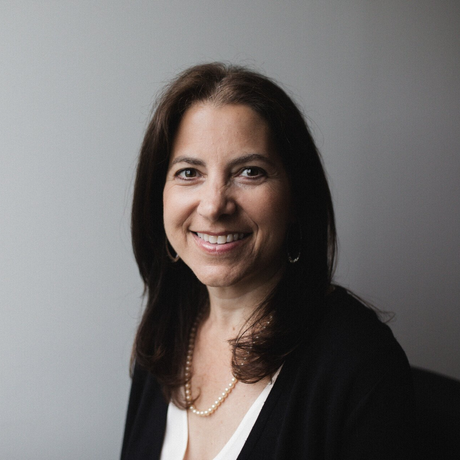 A woman wearing a black sweater and a white shirt is smiling for the camera.