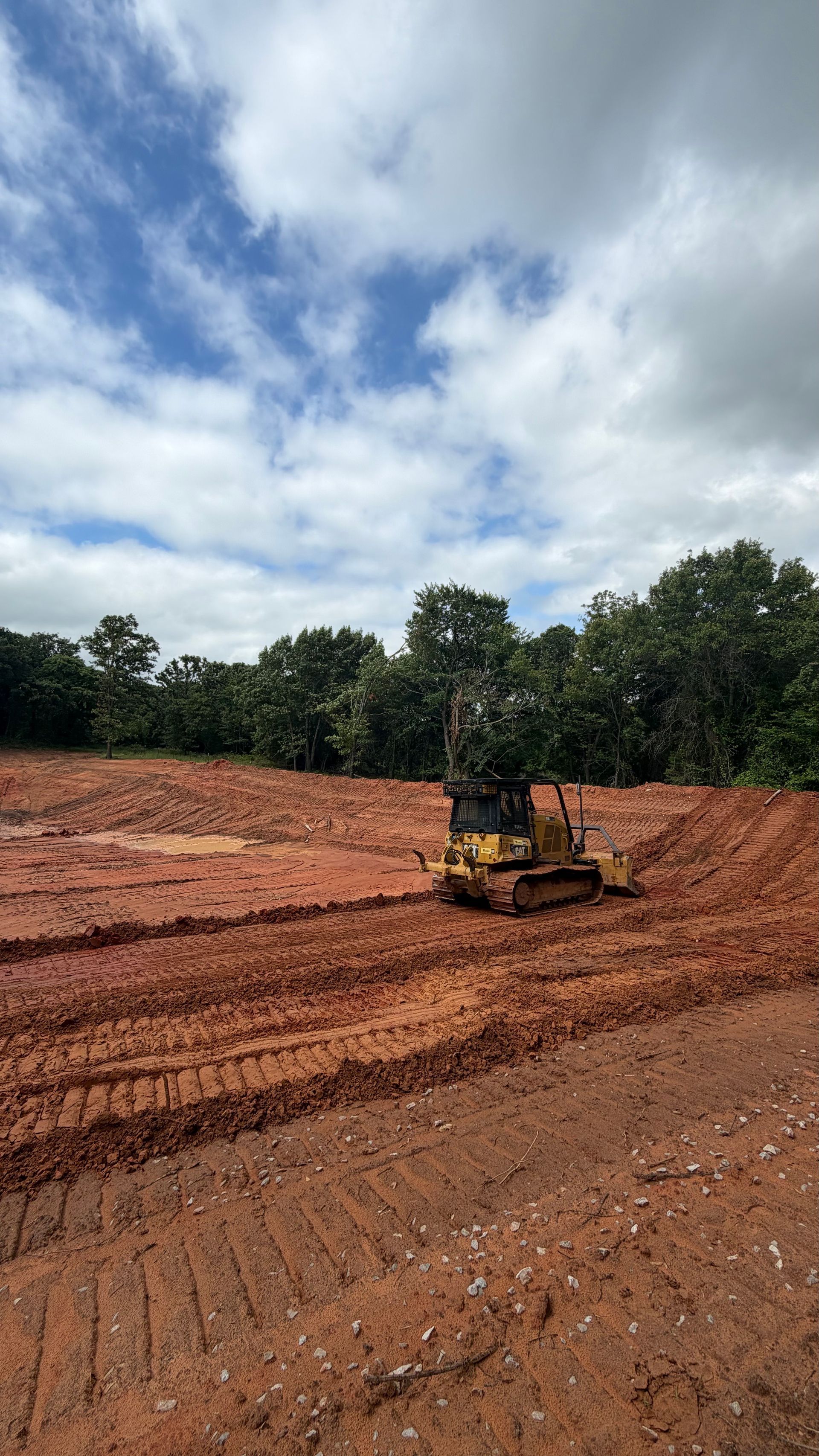 Bulldozer grading a red dirt clearing under a cloudy sky