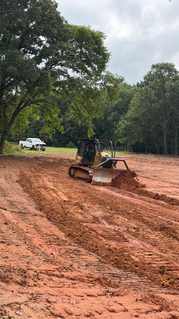 Bulldozer smoothing muddy red soil in a wooded construction area