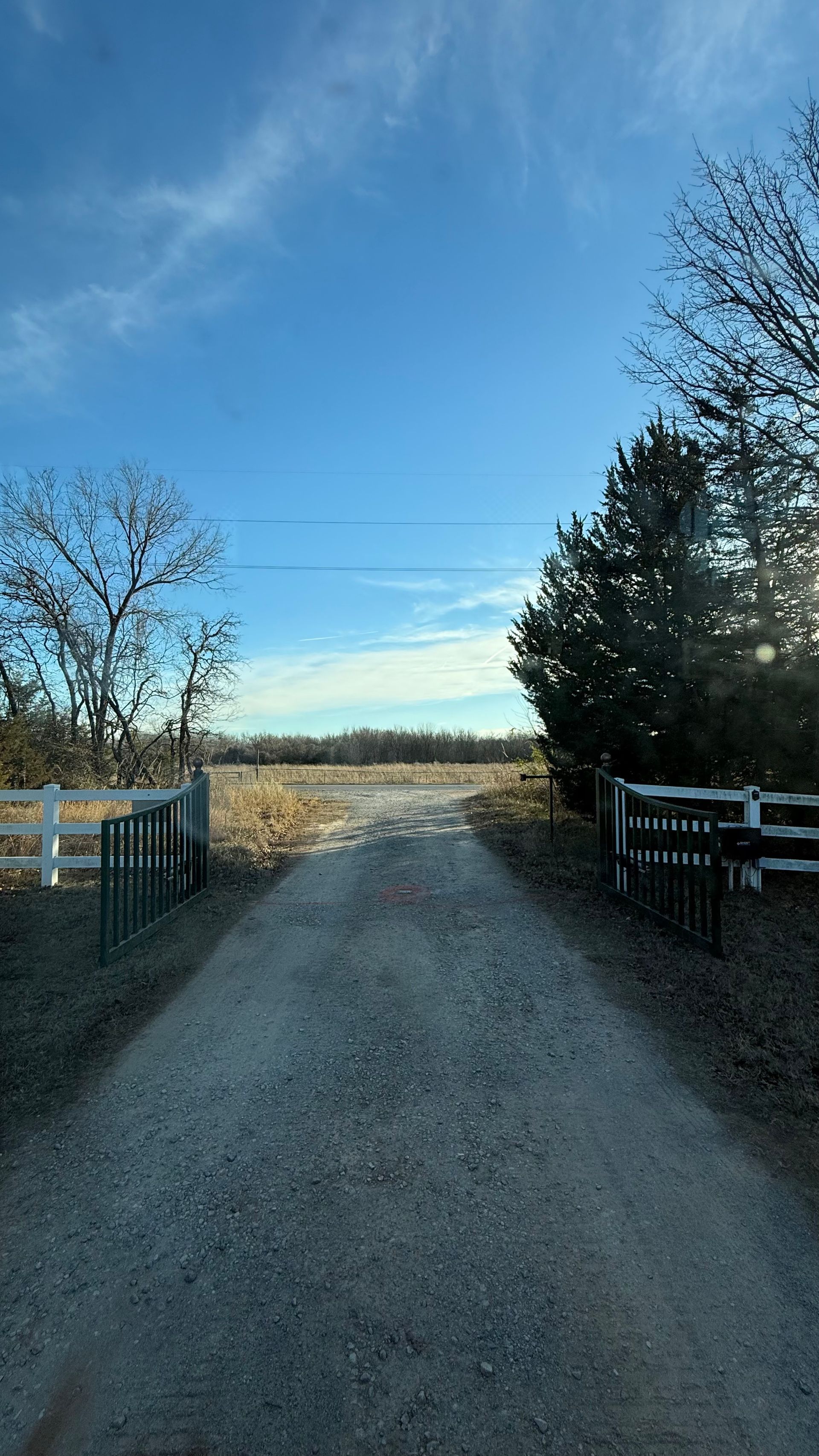 Gravel road leading through open gates toward a bright field under a blue sky