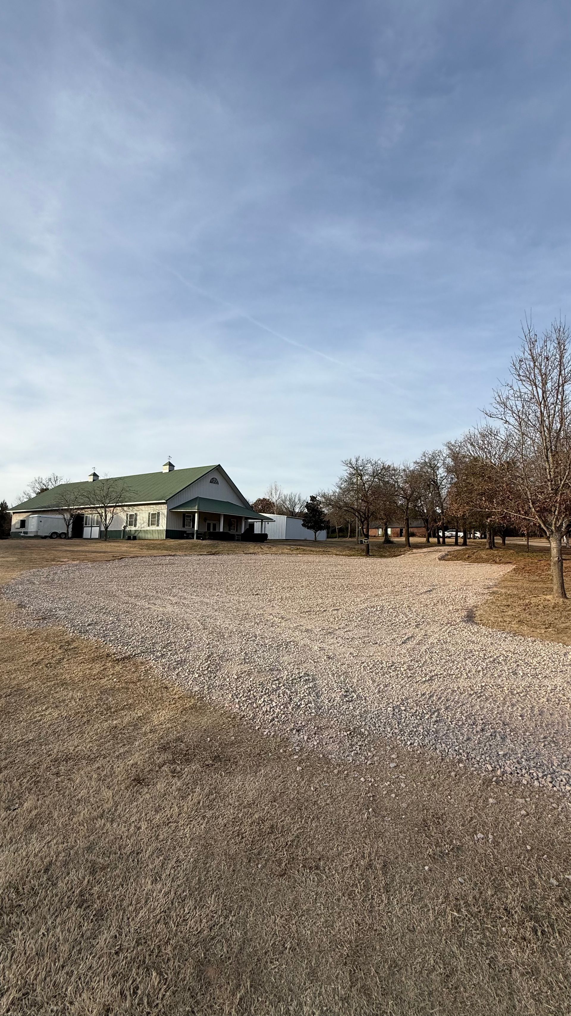 Gravel lot with a small building and leafless trees under a blue sky