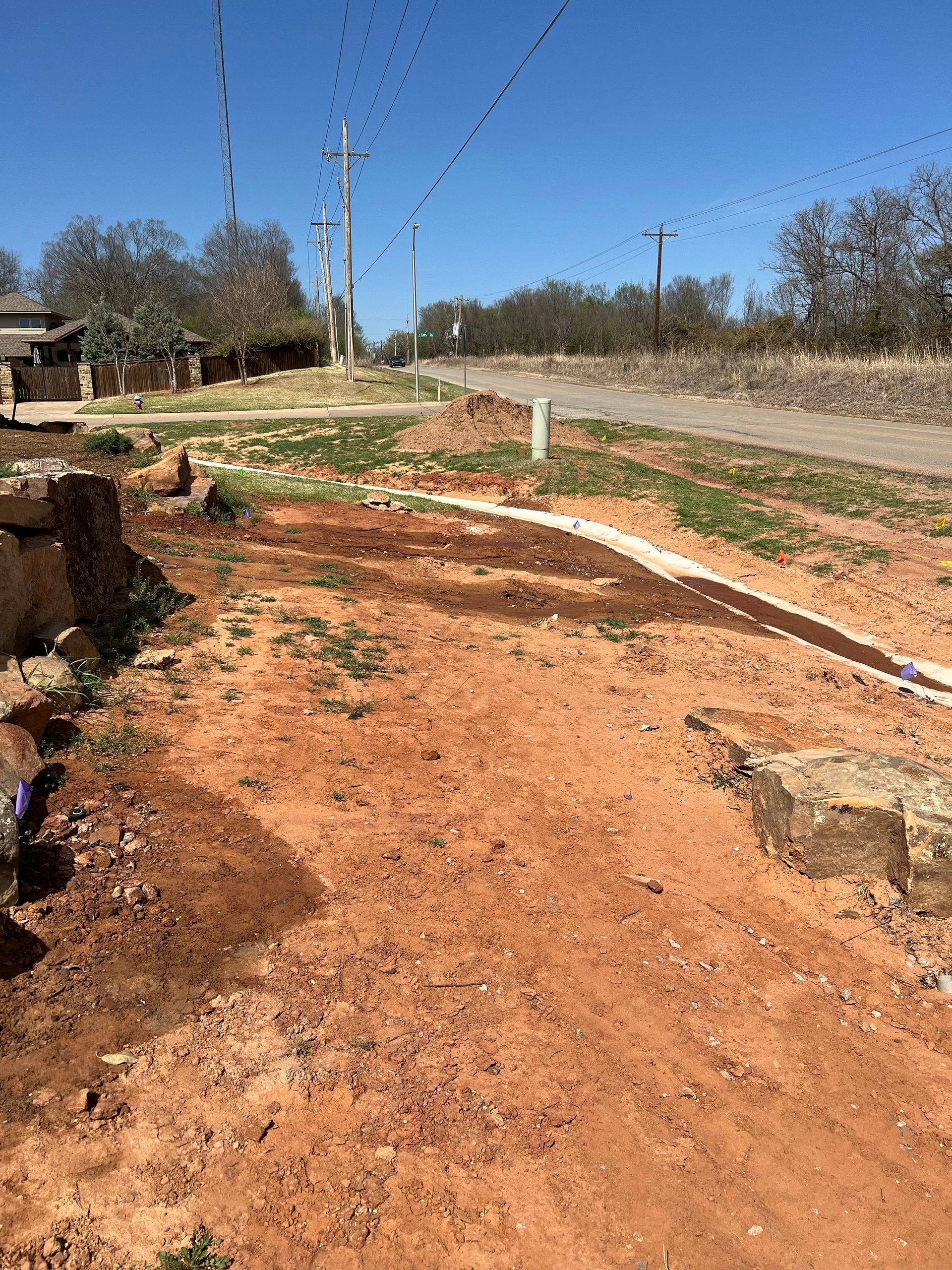 Dirt path beside a gravel road under a blue sky, with utility poles and trees in a rural area