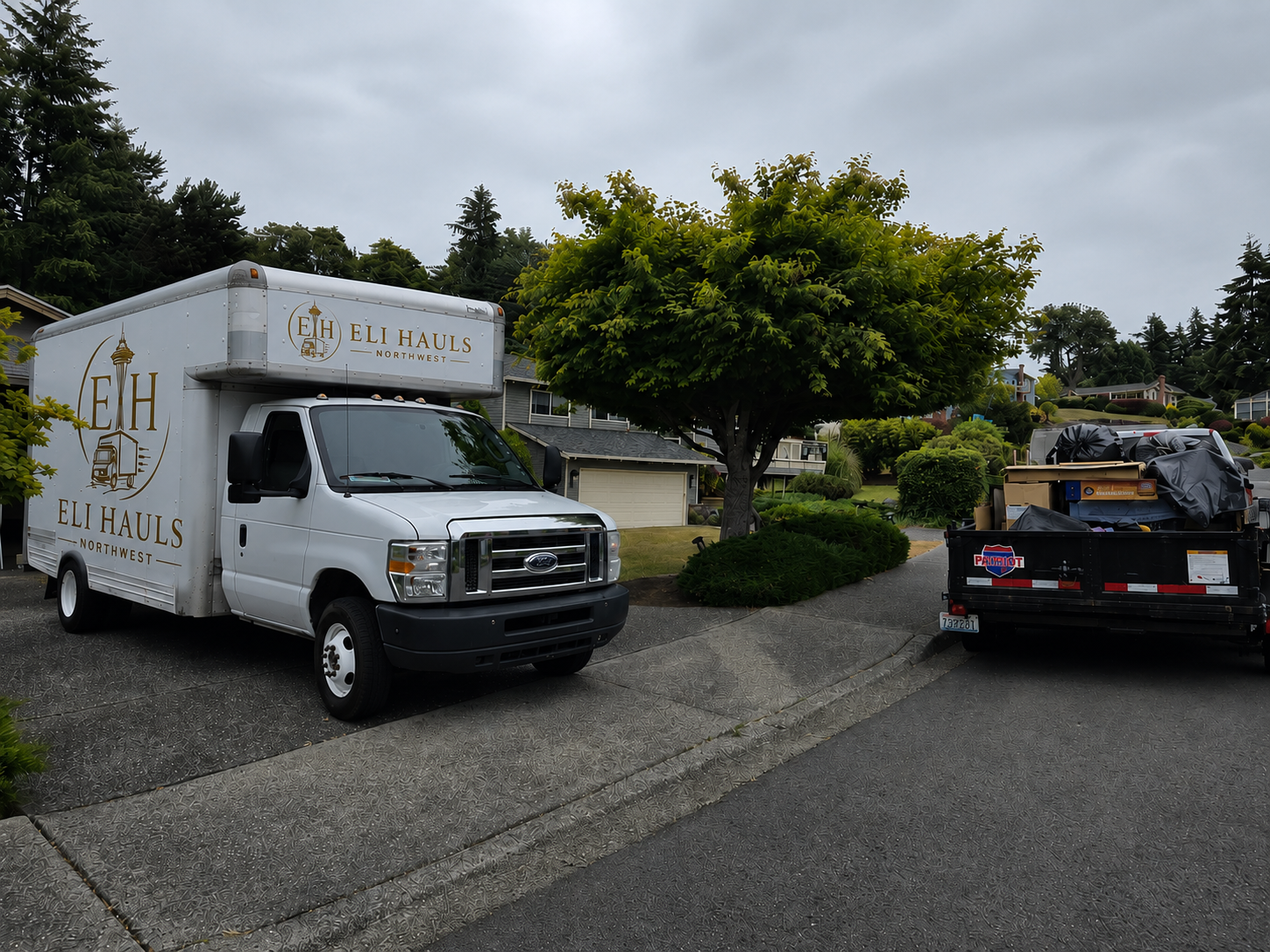 Two trucks parked on a wet residential street, one white box truck and one black pickup loaded with equipment.