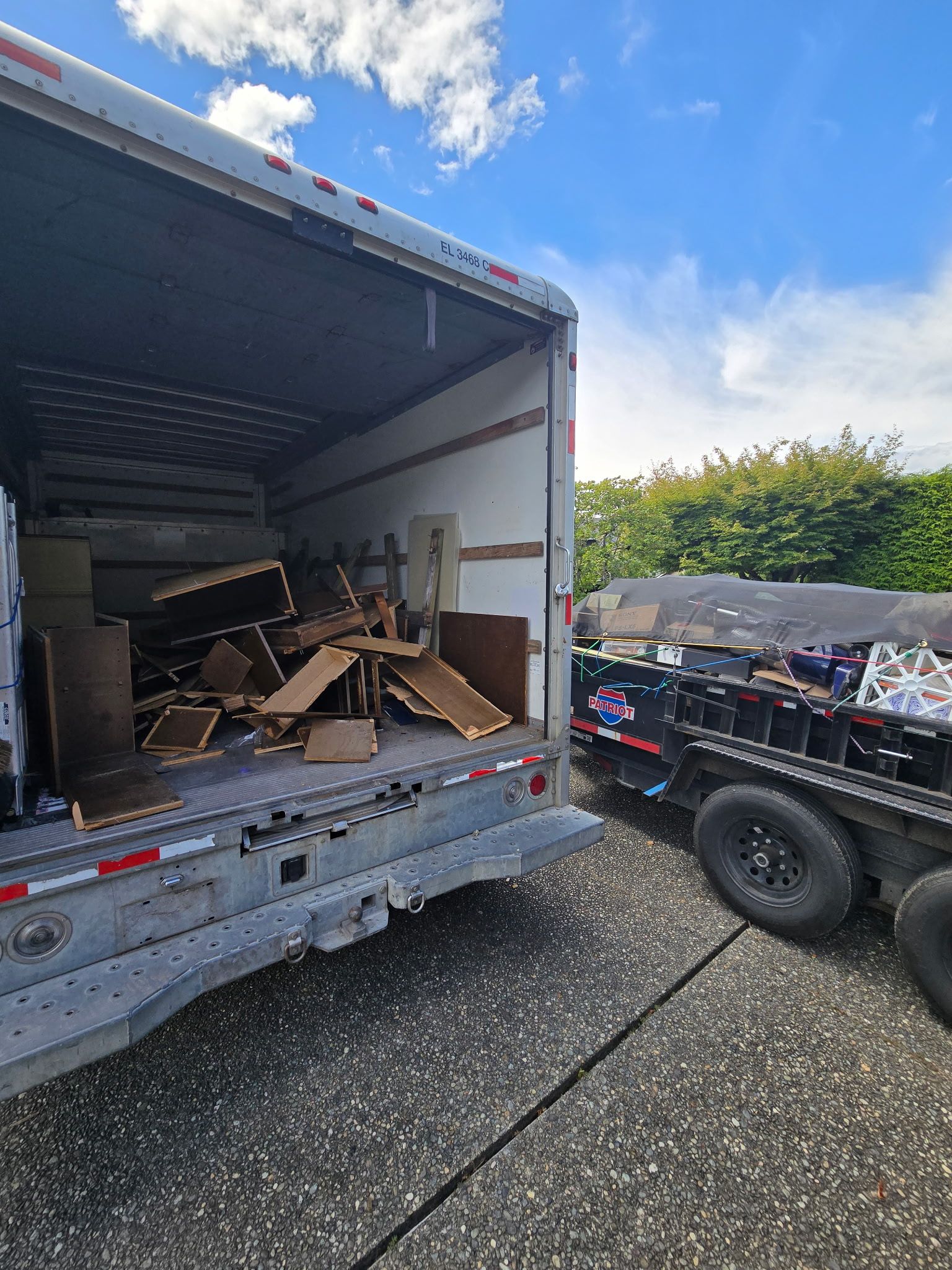 Open trailer loaded with scrap wood beside a small utility trailer on a sunny driveway