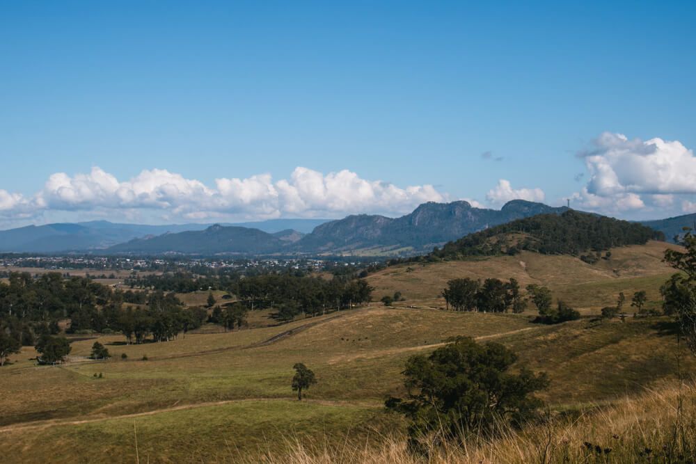 A View Of A Grassy Hillside With Mountains In The Background On A Sunny Day — Bulley Roof Restoration, Painting & Pressure Cleaning in Gloucester, NSW