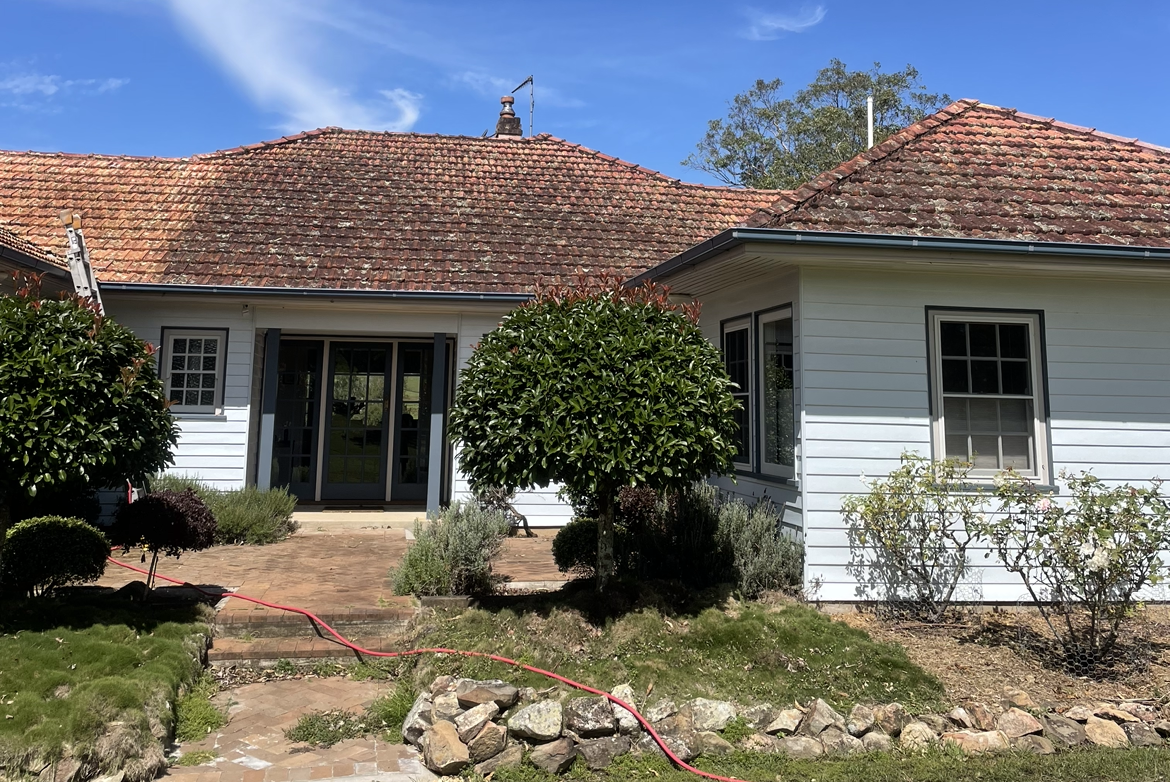 A White House with A Red Tile Roof and A Hose in Front of It Before — Bulley Roof Restoration, Painting & Pressure Cleaning in Wingham, NSW