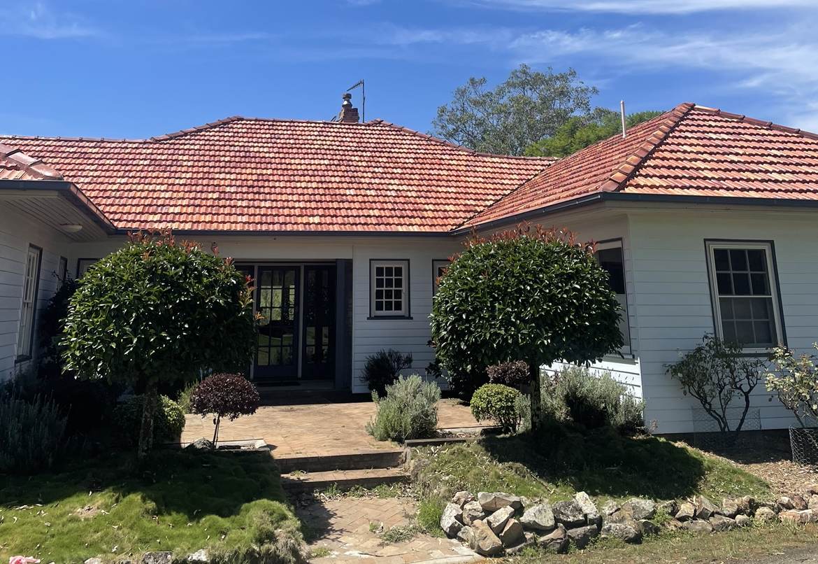 A White House with A Red Tile Roof and Bushes in Front of It After — Bulley Roof Restoration, Painting & Pressure Cleaning in Wingham, NSW