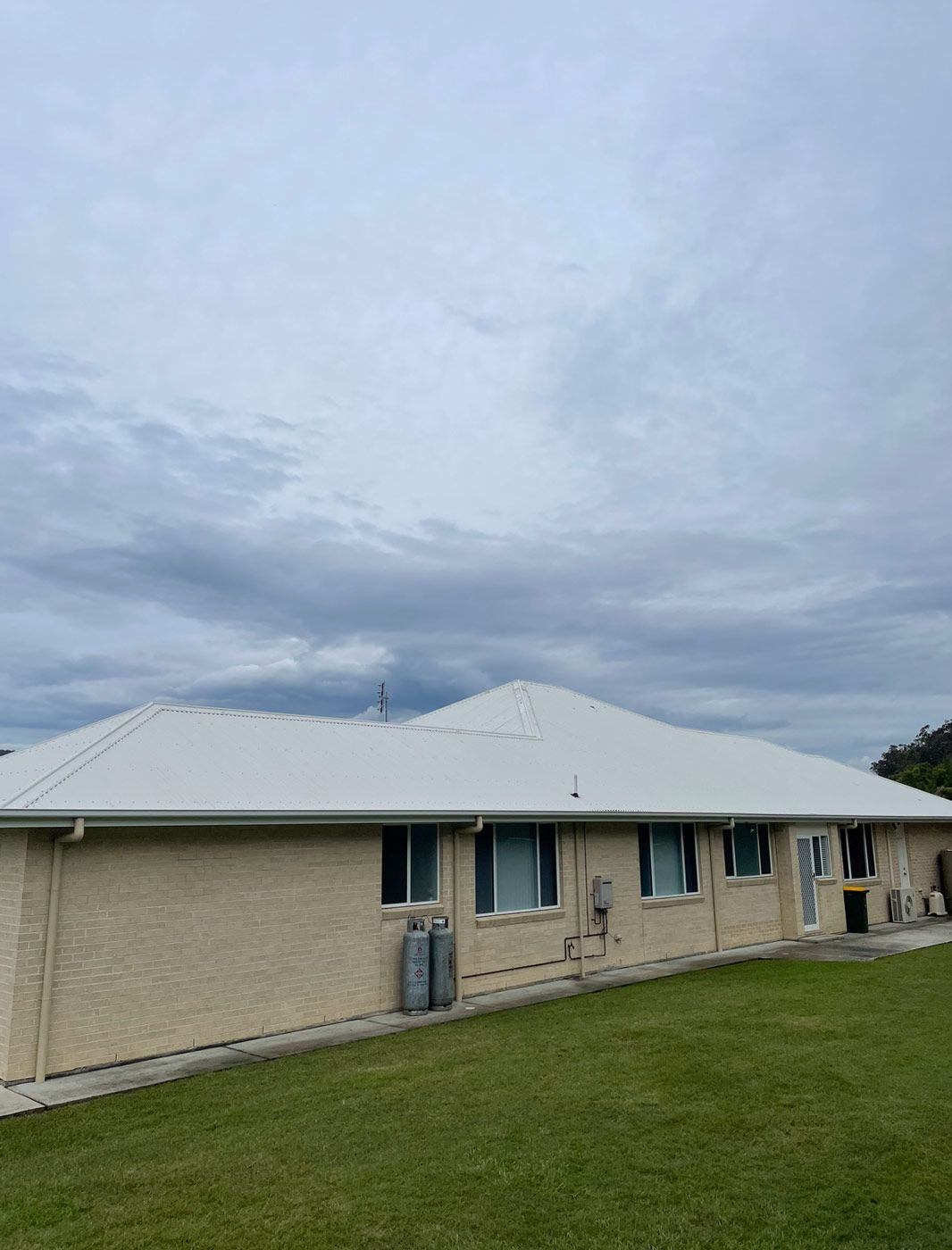 A Brick House With A White Roof And A Large Lawn In Front Of It — Bulley Roof Restoration, Painting & Pressure Cleaning in Forster-Tuncurry, NSW
