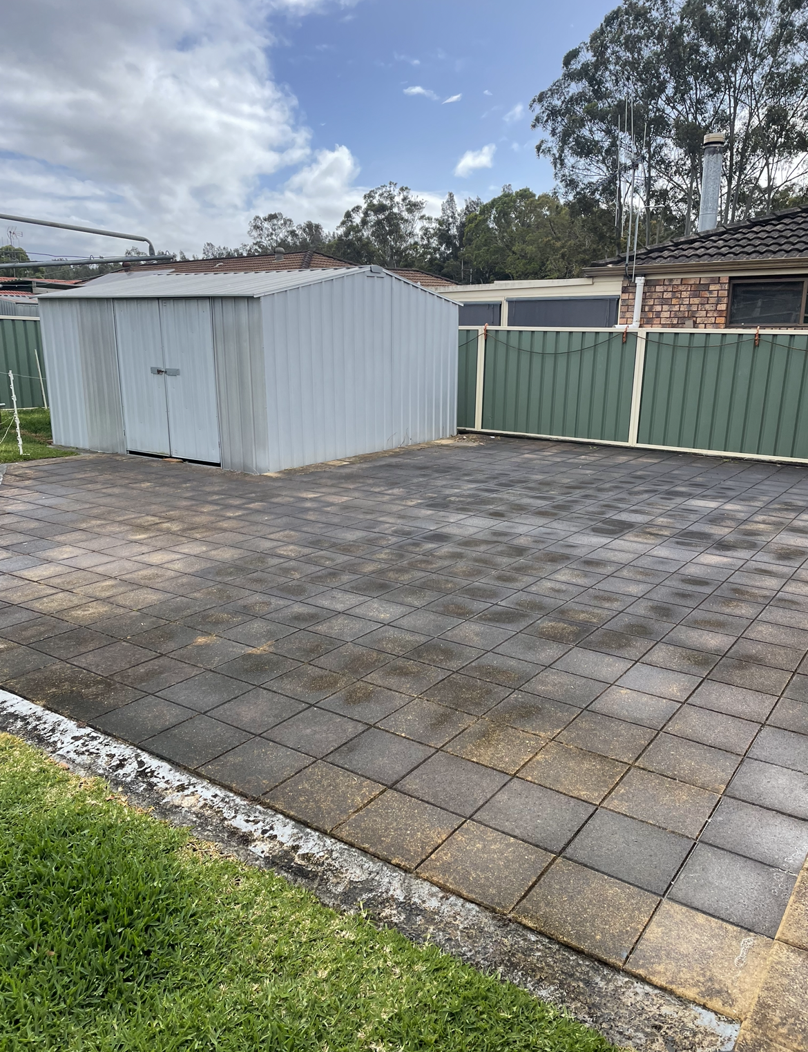 A White Shed Is Sitting in The Middle of A Driveway Next to A Green Fence Before — Bulley Roof Restoration, Painting & Pressure Cleaning in Wingham, NSW