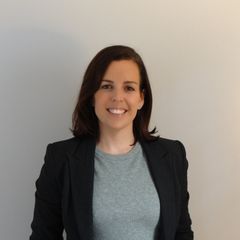 Jessica Smeltink Smiling in a black blazer and gray sweater against a plain light wall