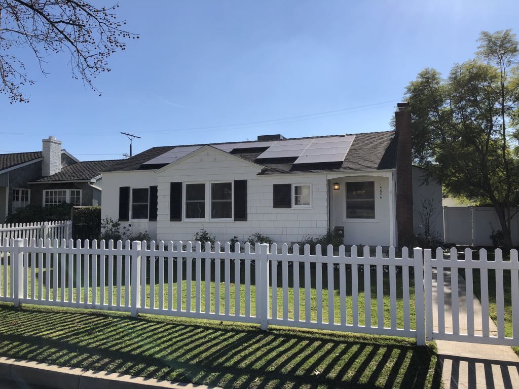 A white house with solar panels on the roof and a white picket fence
