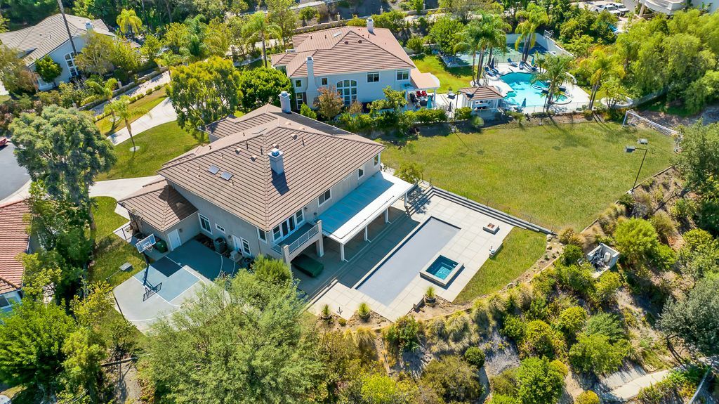 An aerial view of a large house with a pool in the backyard surrounded by trees.