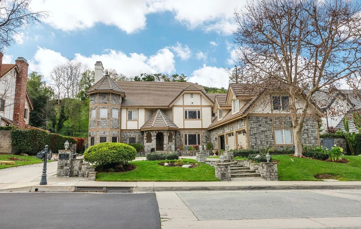 A large house is sitting on top of a lush green lawn in a residential neighborhood.