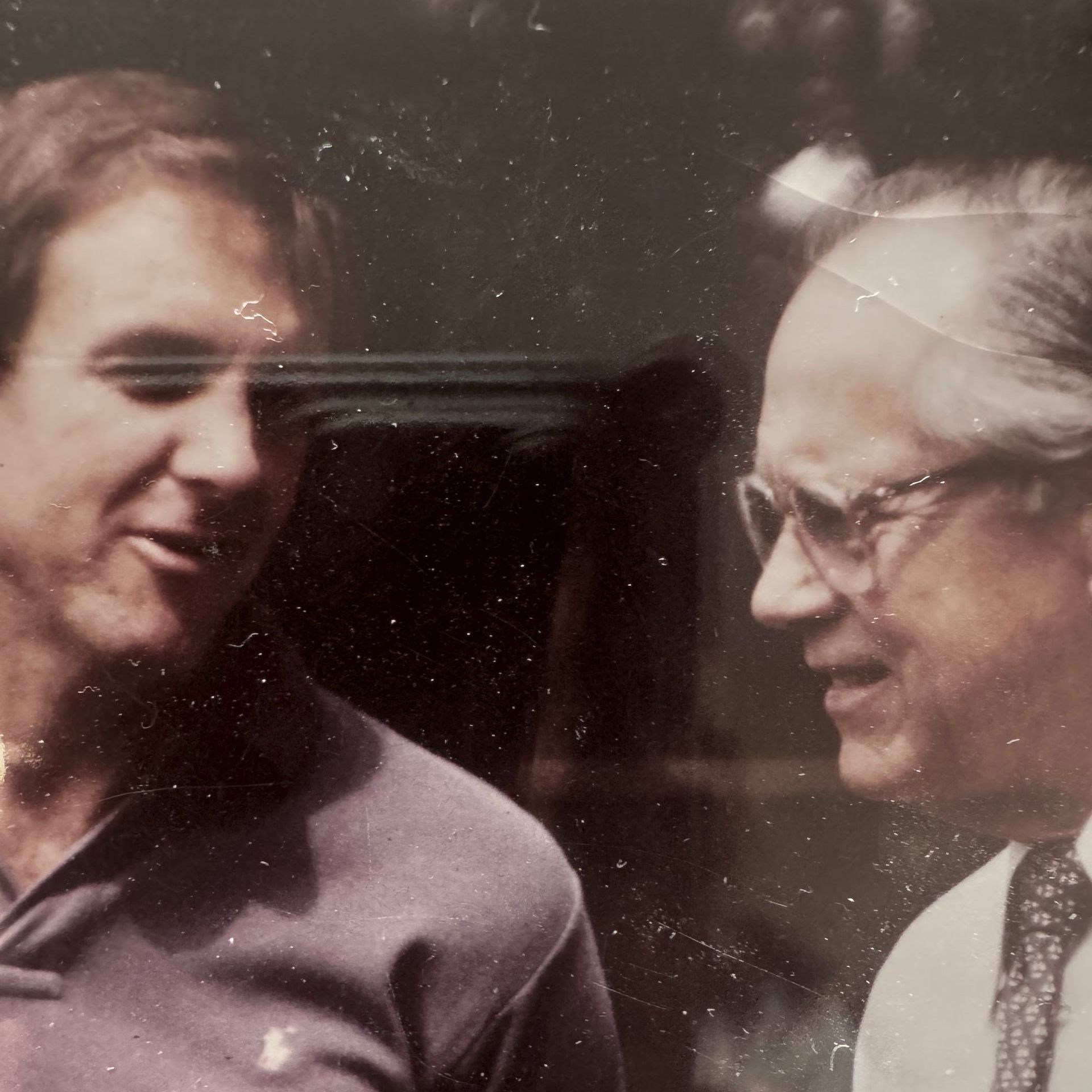 Two men standing next to each other with one wearing glasses