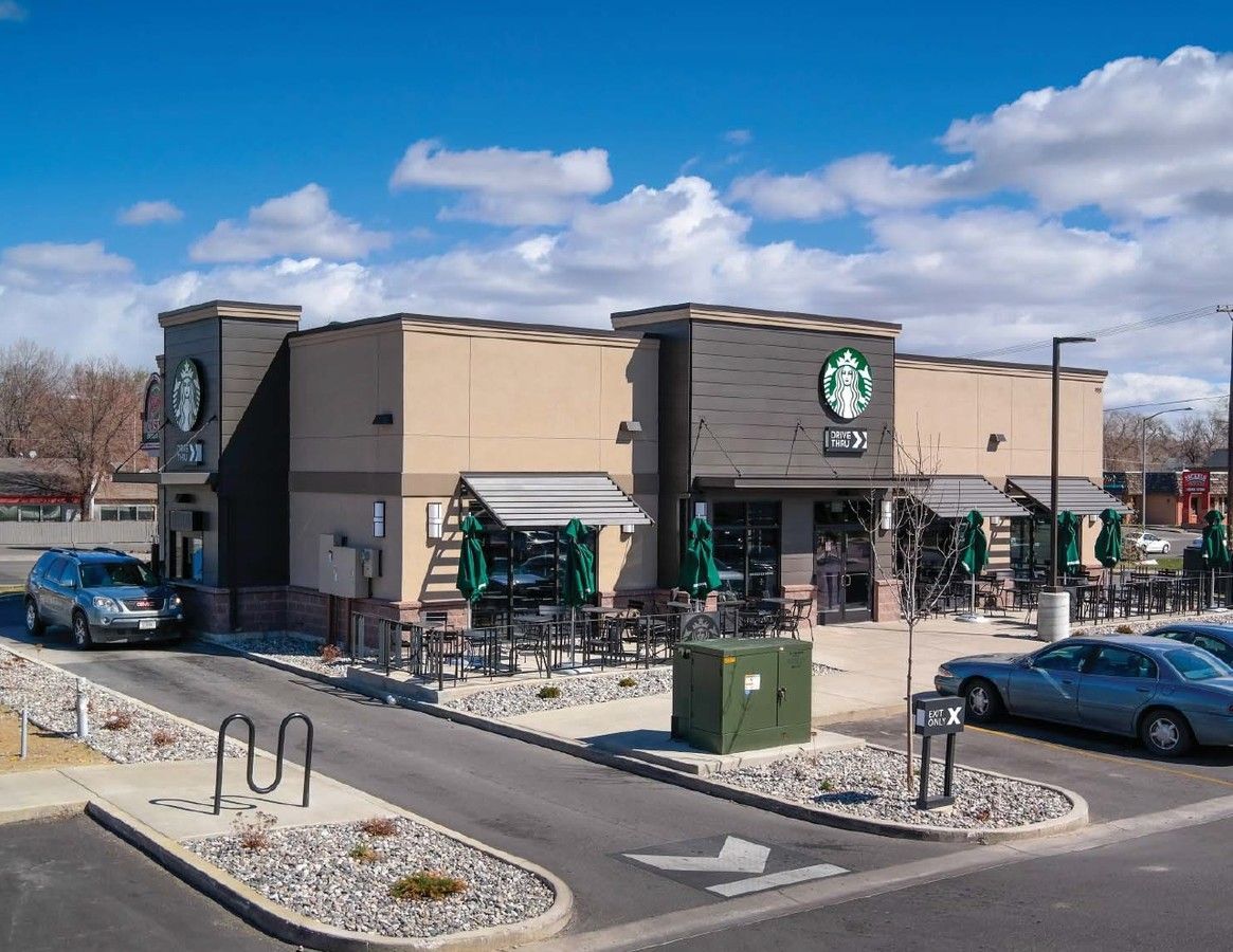 A starbucks coffee shop with cars parked in front of it