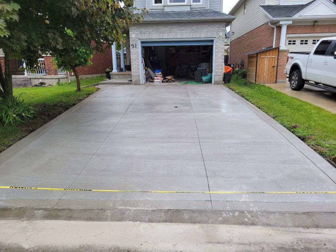 Concrete driveway leading to a house garage, with grass borders and a parked white truck on the right.
